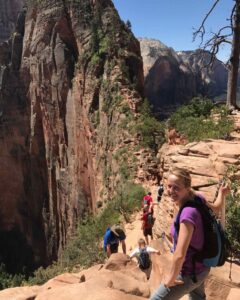 Hiker on Angels Landing trail at Zion National Park with red rock canyon views.