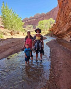 Family wading through a stream in Capitol Reef National Park's red rock canyon.